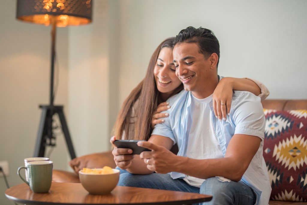 Happy young happy couple using smartphone social media apps at home, smiling husband and wife